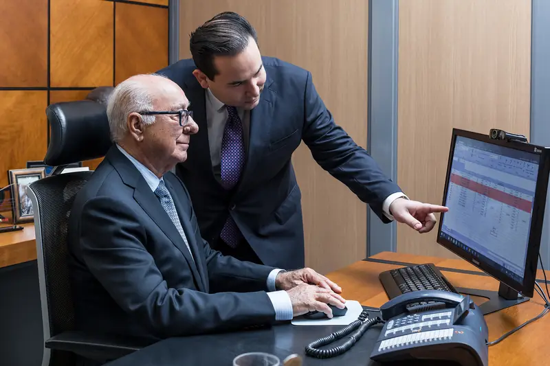 Advogado sentado ao computador enquanto um colega aponta para a tela